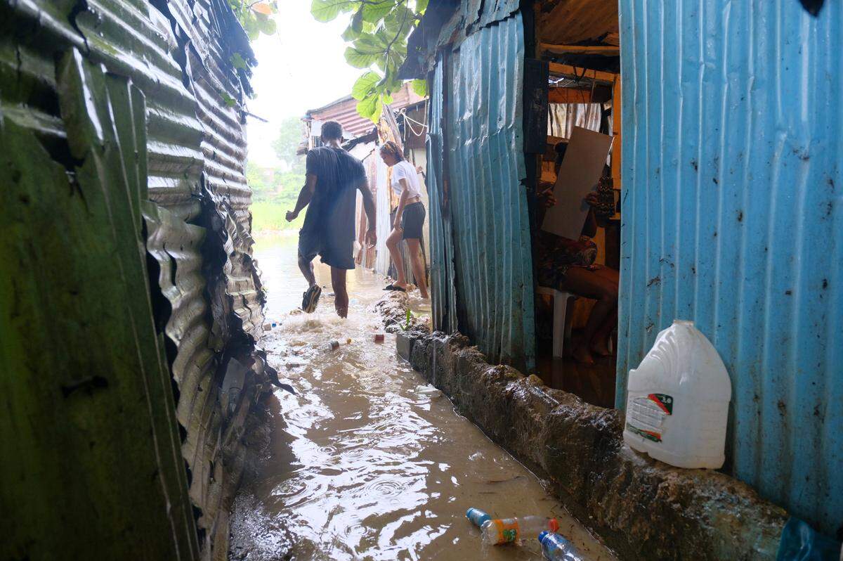 People walk between houses flooded by the rains of Tropical Storm Franklin, along the Ozama River in the Gualey neighborhood of Santo Domingo, Dominican Republic, Wednesday, Aug. 23, 2023.