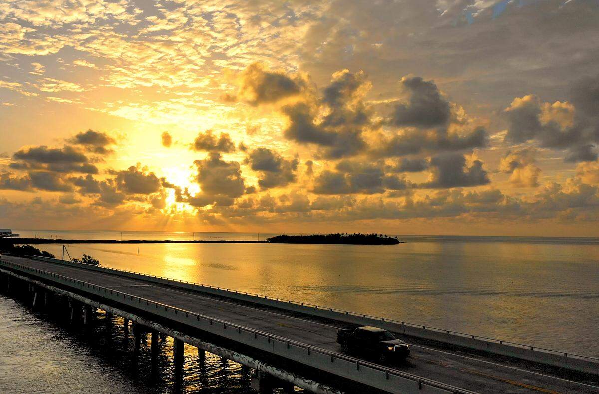 In this aerial photo provided by the Florida Keys News Bureau, a vehicle rolls on the Florida Keys Overseas Highway Monday, Sept. 10, 2018, as the sun rises over the Atlantic Ocean in Islamorada, Fla. A year ago, Category 4 Hurricane Irma pummeled the Keys, leaving major damage for many tourism-related businesses and residents. But, according to Keys tourism officials, the island chain has rebounded with more than 90 percent of the destination’s lodging facilities back in operation, as well as all attractions. (Bob Care/Florida Keys News Bureau via AP)