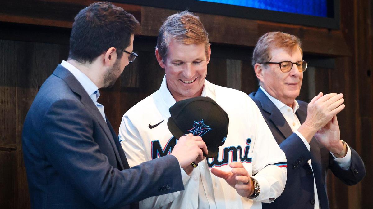 Peter Bendix, President of Baseball Operations, left, gives Clayton McCullough, new Team Manager, center, a jersey and hat while Bruce Sherman, principal owner, claps during a press conference welcoming McCullough to the Miami Marlins on Monday, Nov. 18, 2024, at loanDepot Park in Miami, Fla.