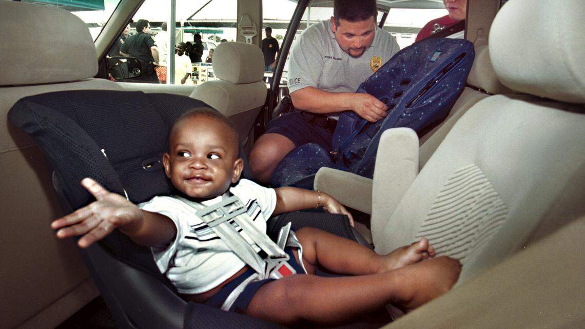 In 2002, 1-year-old Meleek Roberts of Miramar, takes it in stride during a free car seat inspection and safety check by Miramar Police Officer Edgar Gallardo and volunteer Steve McKee, 16.