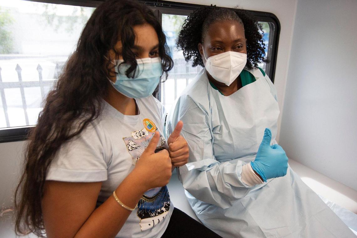 Jenna Ramkhelawan, 12, left, gives a thumbs-up, along with UM Health LPN Delores Fye, after receiving her first dose of the Pfizer vaccine on Tuesday, May 18, 2021. Jenna received her vaccine at a pop-up site run by UHealth’s Pediatric Mobile Unit in an effort to provide free COVID-19 vaccines to uninsured and underprivileged children and parents. The pop-up site was at the Center for Haitian Studies in Little Haiti.