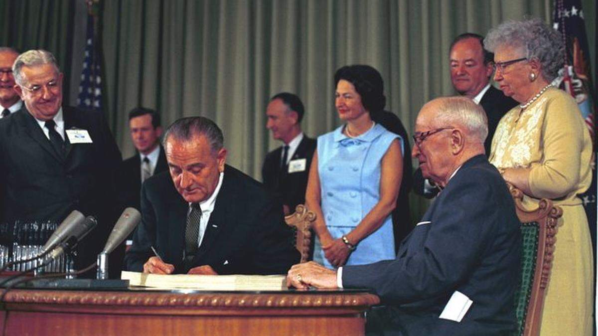In 1965, with former President Harry S Truman sitting beside him, President Lyndon Johnson signed Medicaid and Medicare into law.