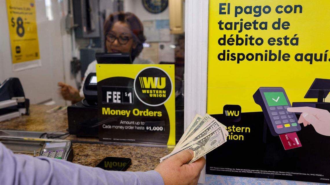 A person holds cash in his hand next to Western Union signs at a Florida Check Cashing window inside a convenience store in Miami, Florida, on January 12, 2023. - (Photo by Eva Marie UZCATEGUI / AFP) (Photo by EVA MARIE UZCATEGUI/AFP via Getty Images)