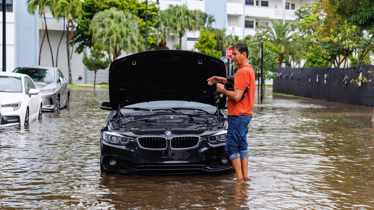 A man stands next to his vehicle stranded on the road flooded due to heavy rain at North Bay Road and 179th Dr. in Sunny Isles Beach on Wednesday, April 25, 2023.