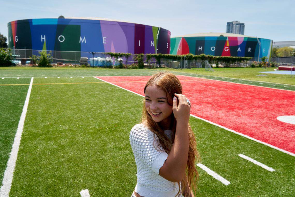 Valentina Mena, a sophomore at Miami Beach Senior High School, in front of the “My Home, Mi Hogar” mural on Friday, May 5, 2023. A line from her poem is featured on the two water tanks.