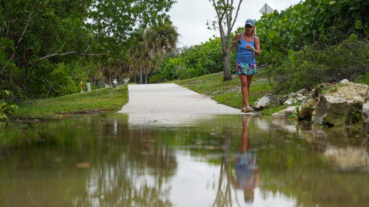 Janice Kmetz of Bonita Springs takes a photo of water from the Vanderbilt Channel flooding a sidewalk as Hurricane Idalia passes Naples during a king tide on Tuesday, Aug. 29, 2023.