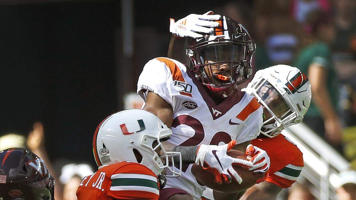 Virginia Tech Hokies defensive back Jermaine Waller (28) intercepts as Miami Hurricanes wide receiver Mike Harley (3) and wide receiver Jeff Thomas (4) tackle him in the first quarter as the University of Miami hosts Virginia Tech at Hard Rock Stadium in Miami Gardens on Saturday, October 5, 2019.