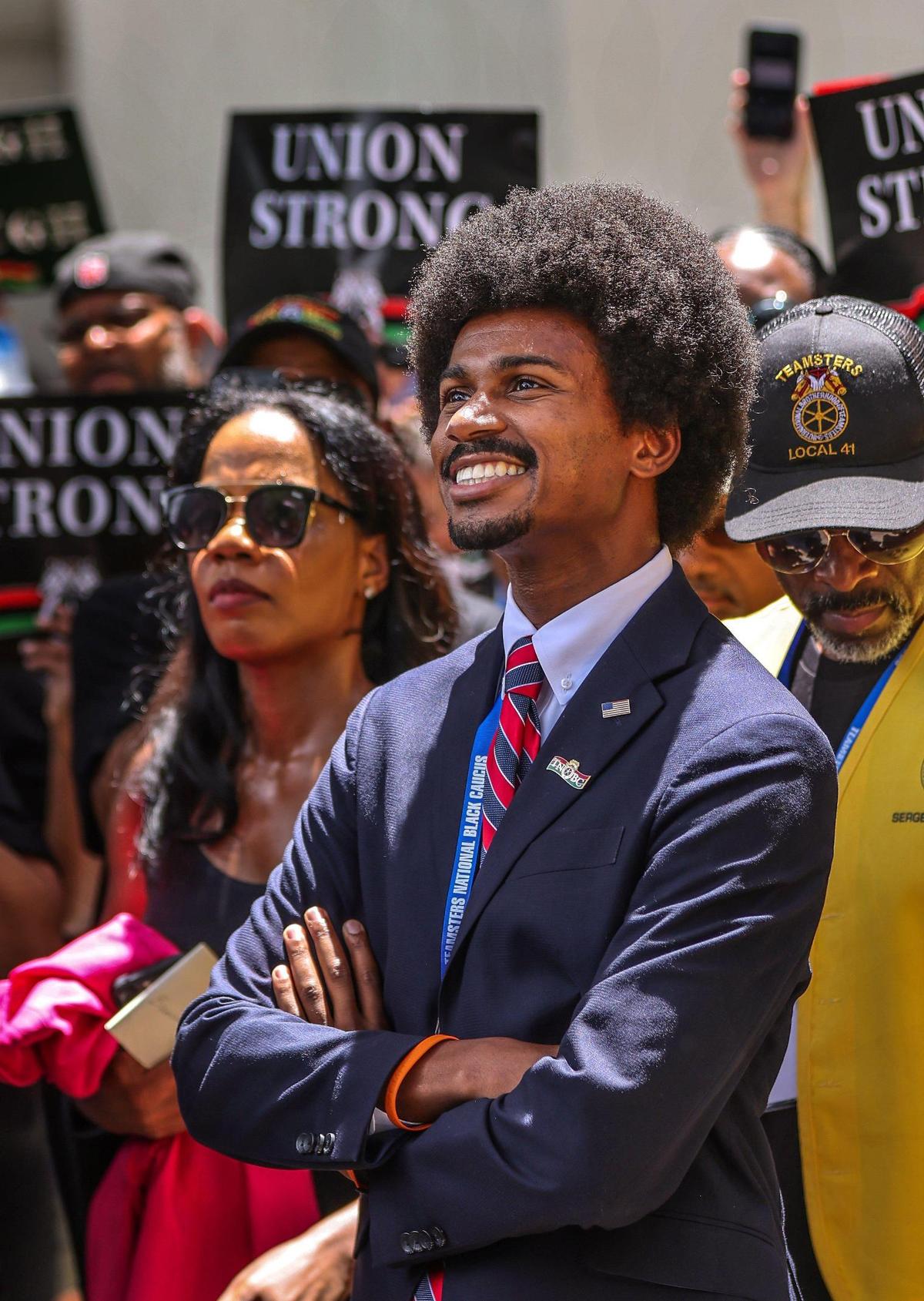 El representante estatal demócrata de Tennessee Justin Pearson, en el centro, sonríe mientras espera para subir al escenario durante la manifestación frente al edificio administrativo de la Junta Escolar del Condado Miami-Dade en una protesta por los nuevos estándares de historia afroamericana aprobados por el estado en julio, el miércoles 16 de agosto de 2023, en Miami, Florida. A la derecha, Marvin Dunn.
