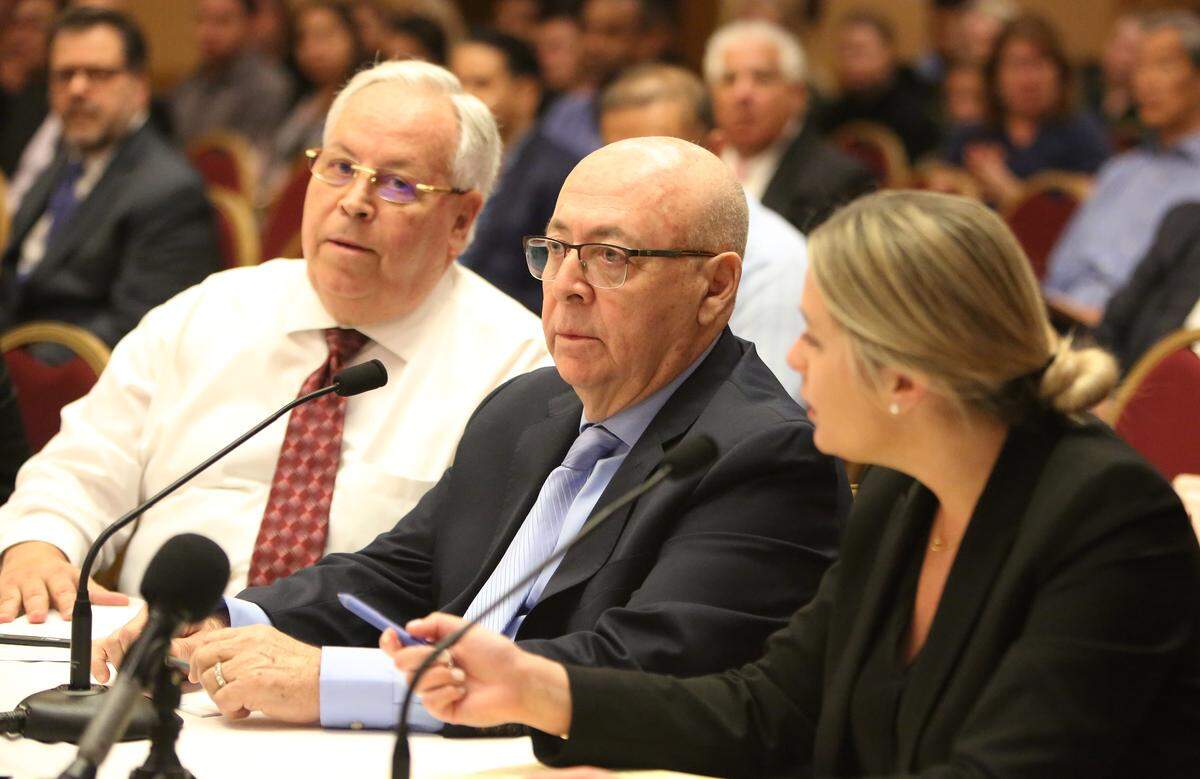Dr. Arnaldo Valls, 75, center, answers questions with the help of interpreter Gustavo Lairet, left, and his attorney, Alison Patino, during a Florida Board of Medicine’s hearing Friday, April 5, 2019, in West Palm Beach. Valls is charged with malpractice after one of his patients died during a Brazilian butt lift in December 2017 and another patient’s intestine was punctured during the same type of surgery in June 2016.
