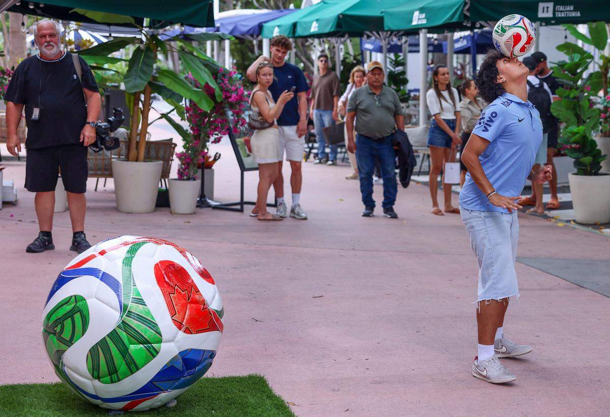 Ricky Martínez, futbolista de la Universidad St. Thomas de 22 años, equilibra un balón de fútbol sobre la cabeza mientras él y otras personas esperan para entrar a la nueva tienda de la Copa Mundial de la FIFA, el lunes en Miami Beach.