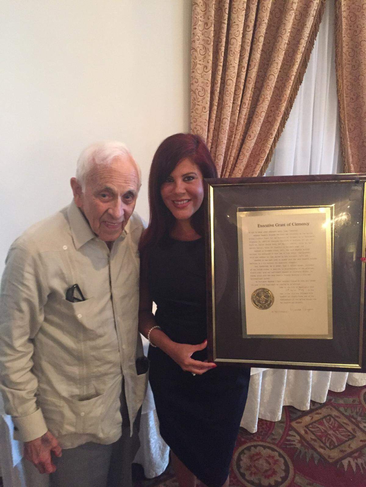 Eugenio Rolando Martínez stands next to his granddaughter, Michelle Diaz, who holds a framed copy of his 1983 pardon by President Ronald Reagan.