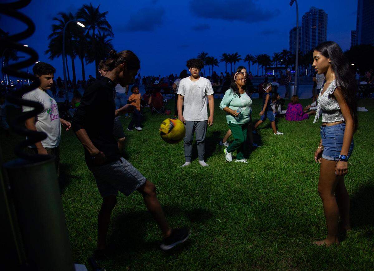Evelyn Lopez (right), 15, watches as Rowin Cruz (left), 16, bounces the ball off his feet before kicking it toward Jender Bencomo (middle), 14, during the Fourth of July Bayfront Park Celebration at Bayfront Park on Tuesday, July 4, 2023 in Miami, Fla.