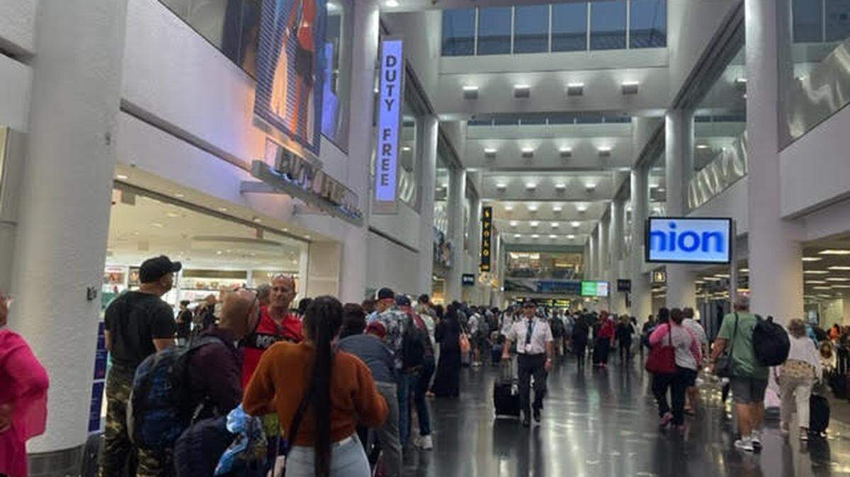 Dozens of passengers stand in line at a Miami International Airport terminal Sunday, July 16, 2023.