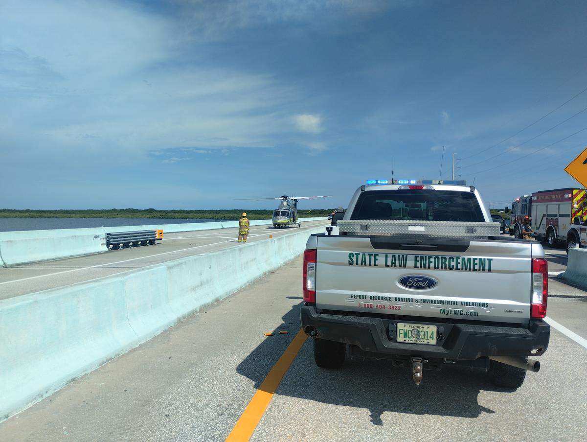 A Florida Fish and Wildlife Conservation Commission police truck is parked on the 18 Mile Stretch of U.S. 1 with a Miami-Dade Fire Rescue helicopter in the distance, Wednesday, Aug. 20, 2025. An FWC officer is being credited with saving a woman who was trapped in her overturned car on the side of the highway.