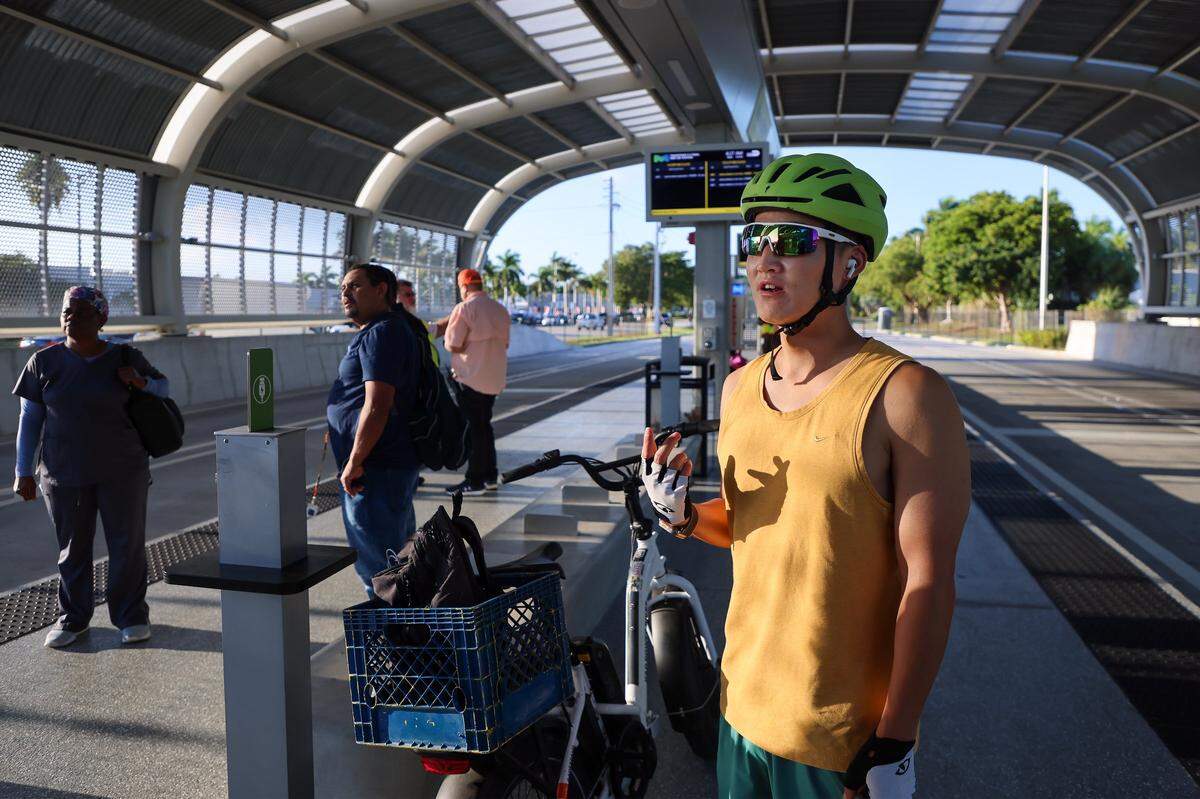 PhD. student Kevin Larson, 28, waits for an empty express bus after several crowded and local buses passed through the 152 Street Station during his first attempt in trying the new express bus line while commuting by electric bike and other forms of public transit on the first day of Miami-Dade's $300 million rapid-transit bus line known as “Metro Express” on Monday, October 27, 2025, just west of Richmond Heights on Coral Reef Drive and U.S. 1. Many first day riders complained about crowded buses and long travel times due to red lights on the express lane. Larson was hoping to measure the time saved by using the new express bus line.