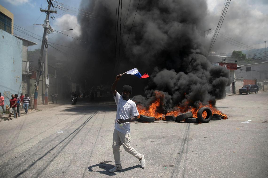 A man waving a Russian national flag as he hopes for support from the Russian government, walks past a burning barricade set up by protesters demanding that Haitian Prime Minister Ariel Henry step down and a call for a better quality of life, in Port-au-Prince, Haiti, Wednesday, Sept. 7, 2022.