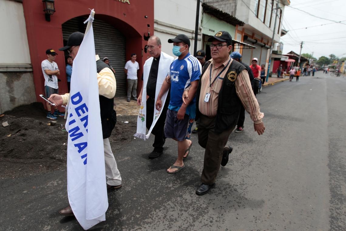 Edwin Roman, parish priest of the San Miguel church, and Danilo Martinez, a member of the Nicaraguan Association for Protection of Human Rights (ANPDH), transport a police officer captured by protesters to the local police station in Masaya, Nicaragua, on June 6, 2018. Álvaro Leiva Sánchez, executive director of the association, walks out front holding a "Human Rights" flag.