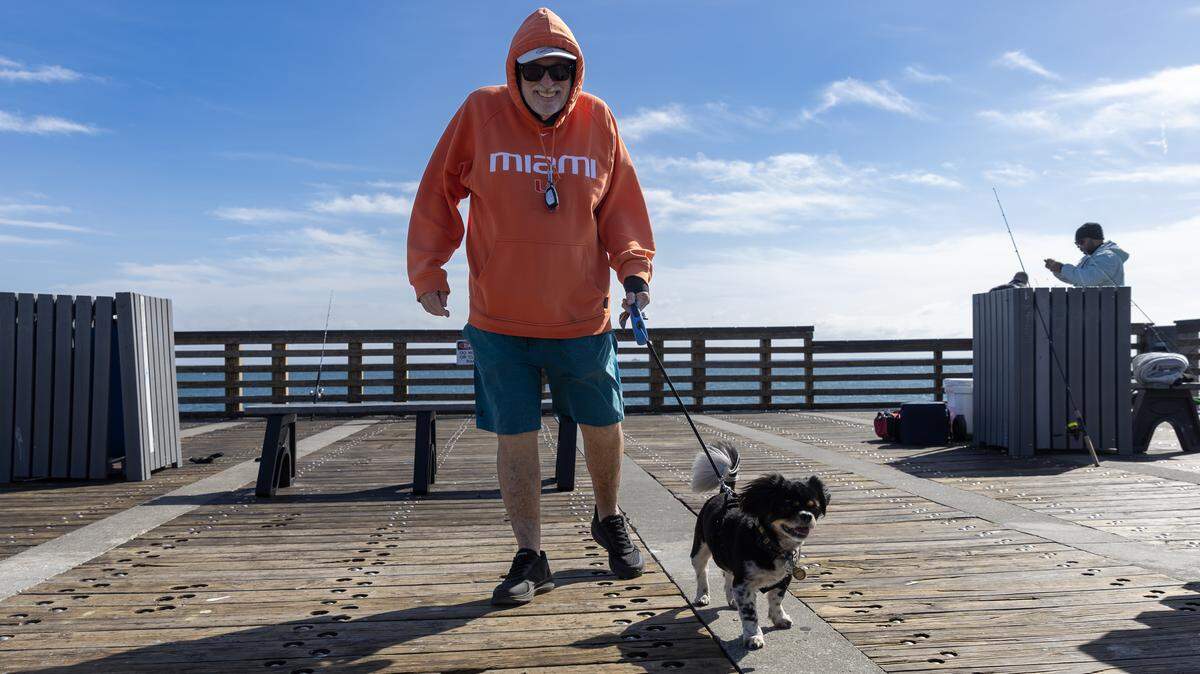 Paul Rich and his Puerto Rican rescue dog from Hurricane Maria, Paco, enjoy the cool morning air at Dania Beach Pier on Nov. 11, 2025, in Dania Beach, Fla. No rain is forecast into Thanksgiving week and temps should be comfy 80s down to 60s.