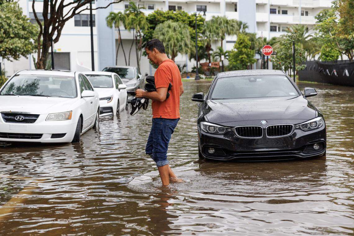 A person stands next to his vehicle stranded on the flooded road due to heavy rain at North Bay Rd and 179th Dr. in Sunny Isles Beach on Wednesday, April 25, 2023.
