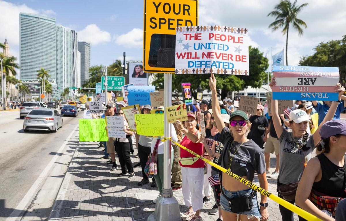 Samantha Renshaw, bottom-right, holds a sign while attending a National Day of Action protest against President Donald Trump and his administration at the Torch of Friendship on Saturday, April 19, 2025, in downtown Miami, Fla.