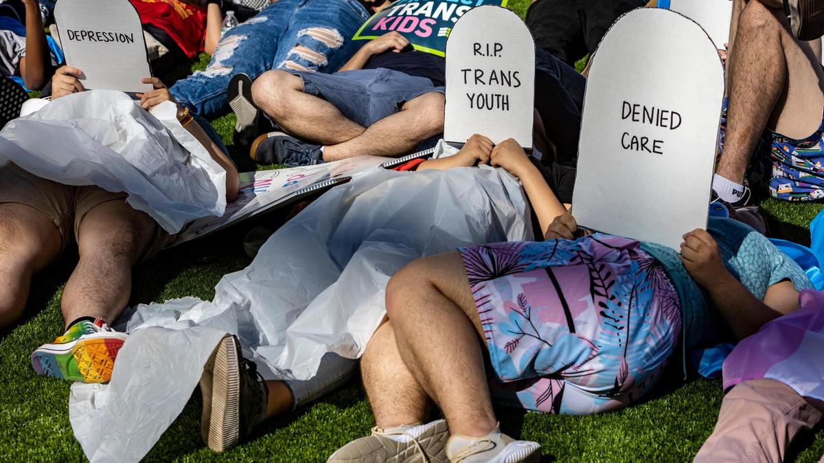 Protesters lie on the ground holding cardboard signs shaped like tombstones in front of the Marriott Fort Lauderdale Airport as the Florida Board of Medicine meets inside. On the agenda is a discussion about a proposed rule by the DeSantis administration to ban doctors from performing gender-affirming surgeries or providing puberty blockers to transgender minors.