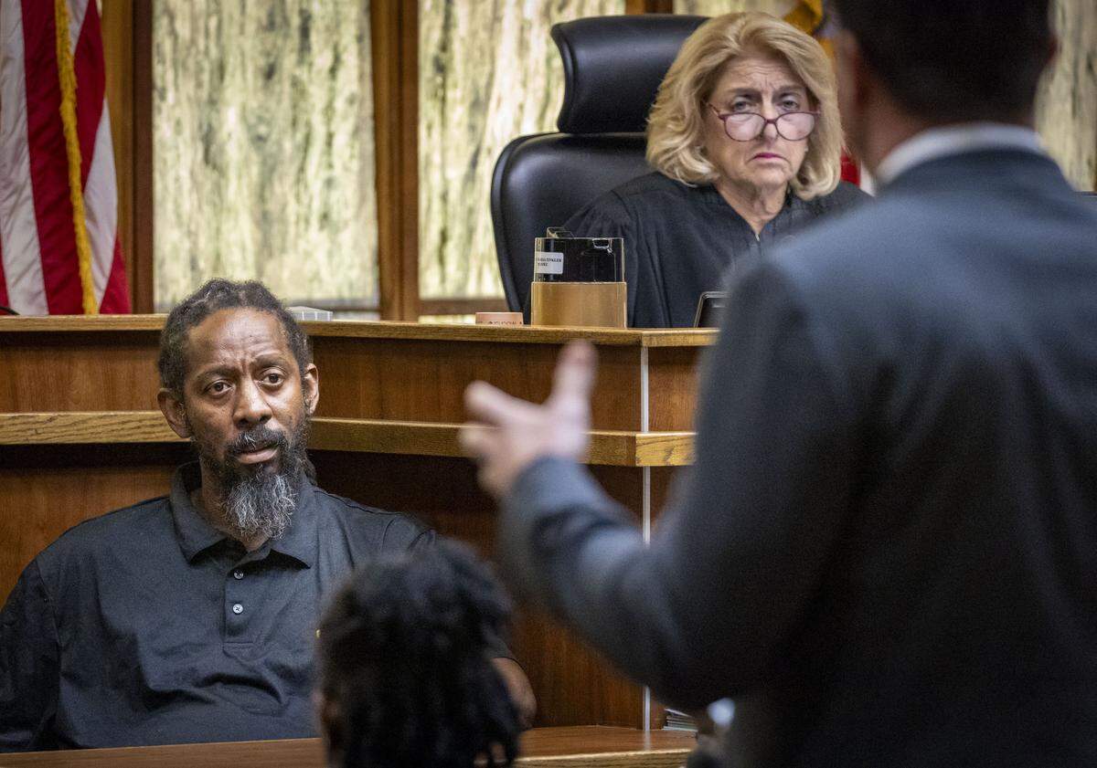 Miami, FL, October 28, 2025 - Under the watch of Judge Marisa Tinkler Mendez, top right, Michael Dennis Jr, Labrant Dennis' brother, left, answers questions from prosecuting attorney Shawn Abuhoff, back to the camera, during court proceedings at Miami-Dade Criminal Court.  Jurors will decide if Labrant Dennis, convicted of fatally bludgeoning his ex-girlfriend and a UM football player she was seeing, will be sent back to Florida's Death Row. 