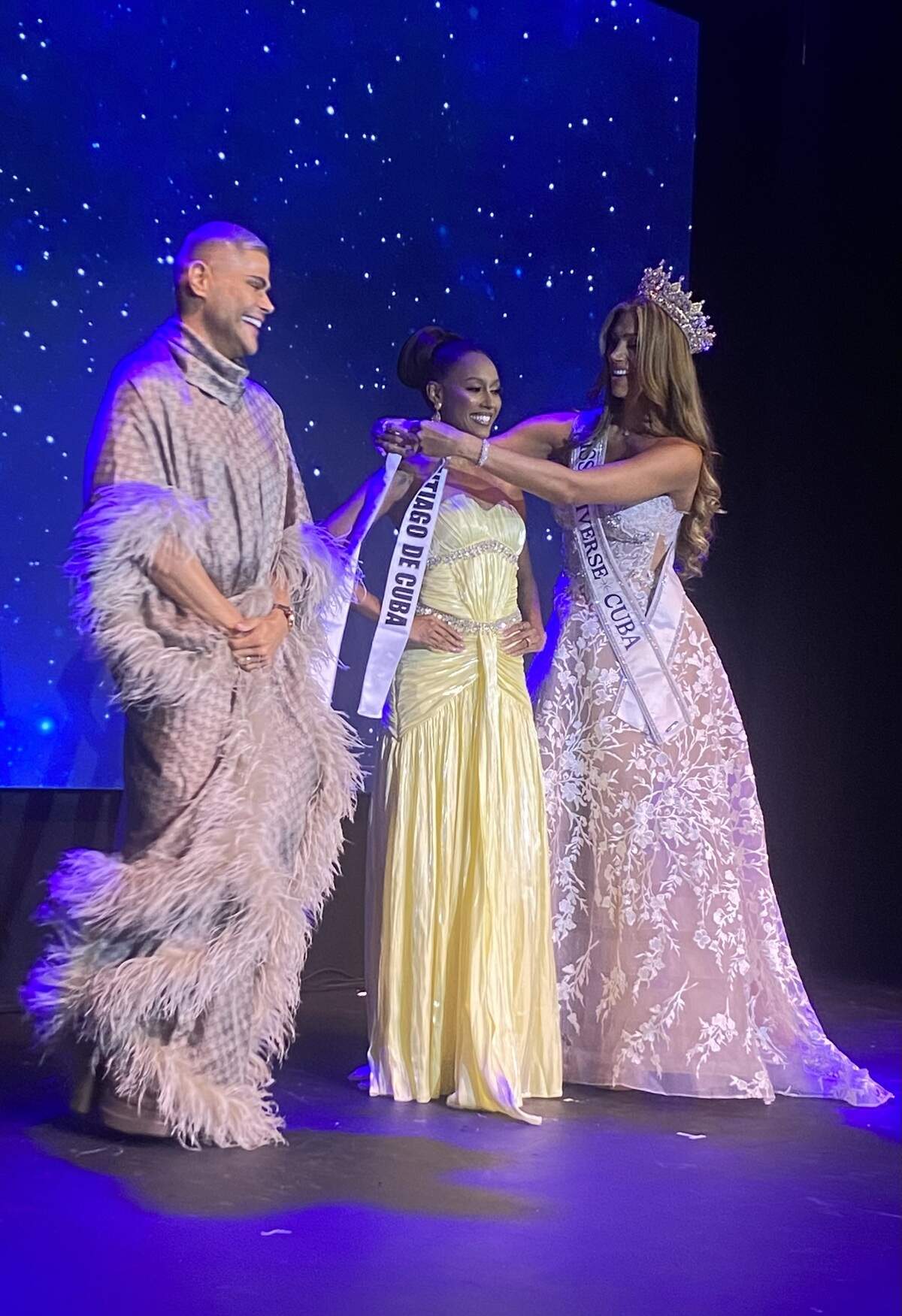 Prince Julio César, director of Miss Universe Cuba, and Lina Luaces, Miss Universe Cuba 2025, place the Santiago de Cuba sash on Regla Díaz.