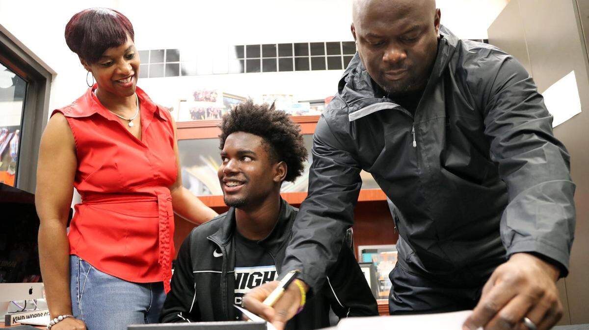 Davonte Brown, 18, smiles as his father, Selwyn Brown, signs the contract for him to play football at UCF and his mother, Renee Brown, stands by his side during signing day at American Heritage School in Plantation on Wednesday, Dec. 18, 2019. ...