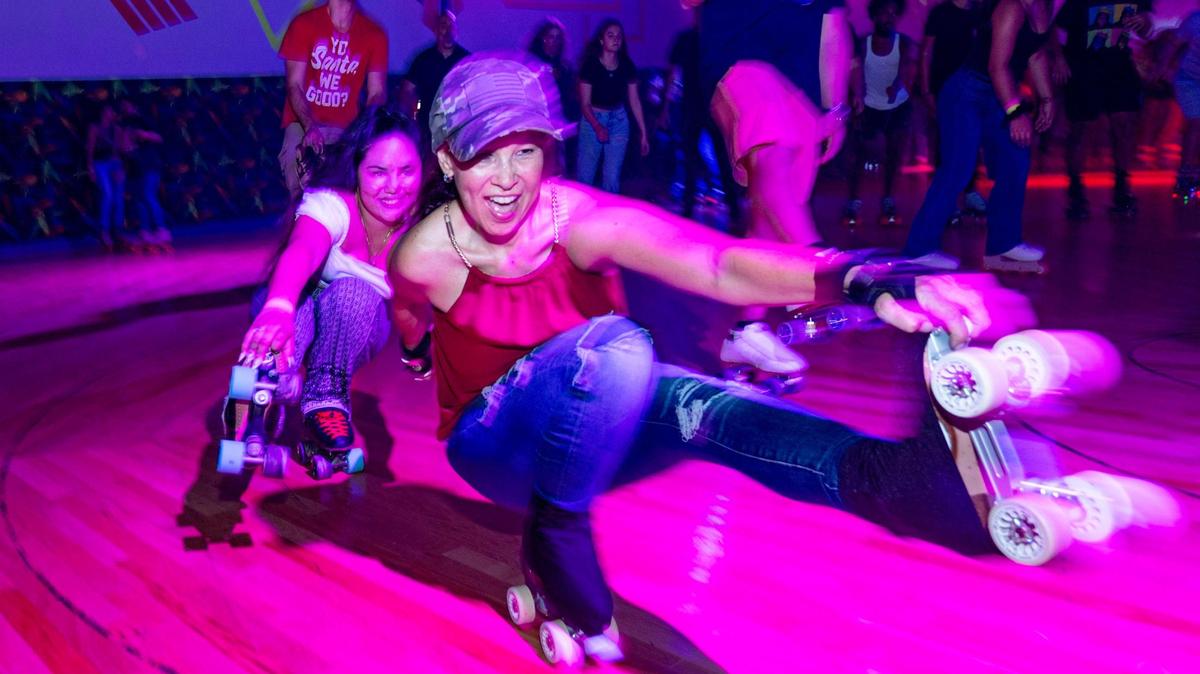 Two roller-skaters perform skate tricks around the roller rink during a skating party to mark the official closing at Super Wheels in Miami, Florida, on Saturday, November 25, 2023.