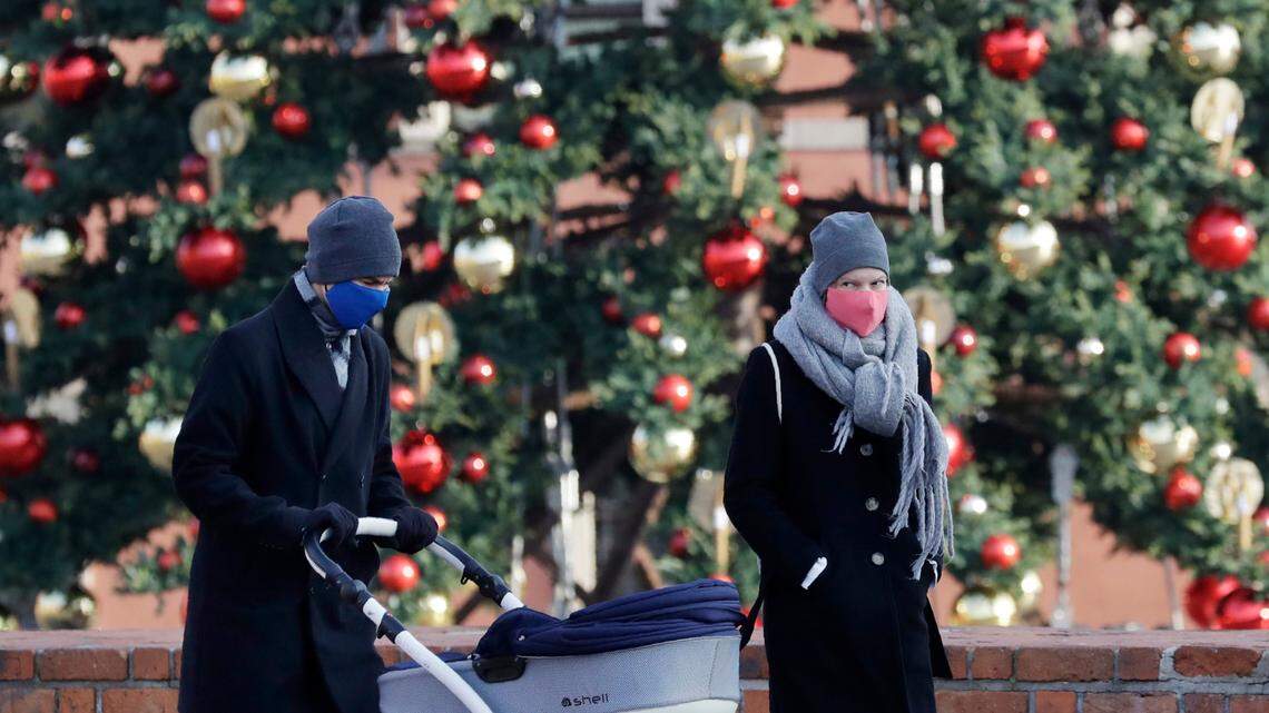 A couple wearing face masks walks by a decorated Christmas tree in Warsaw, Poland, on Dec. 3, 2020. Experts advise caution as families decide whether to gather this holiday season with the spread of the omicron coronavirus variant.