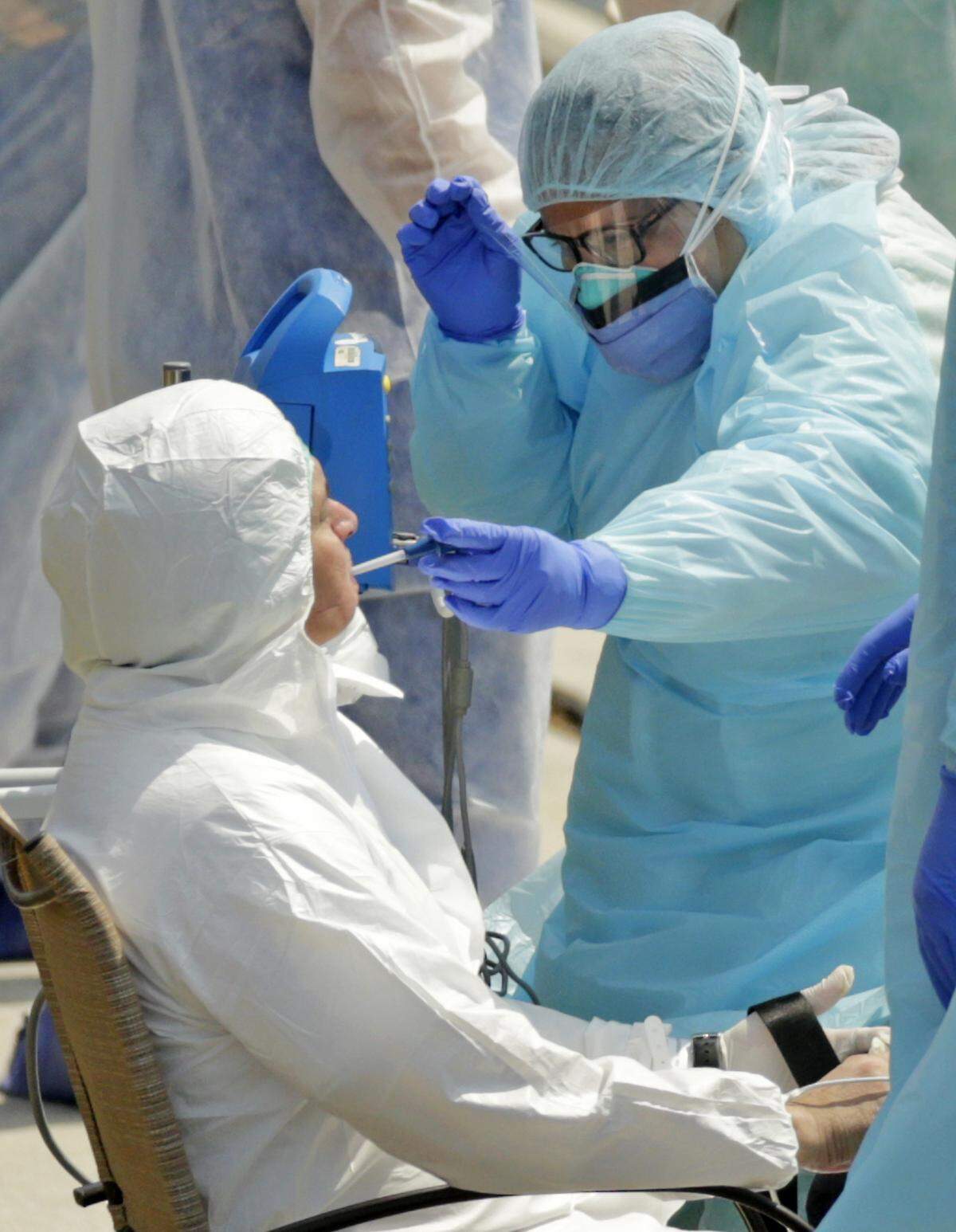 A healthcare worker prepares a crew member said to be showing COVID-19 symptoms for transport after arriving from the cruise ship Costa Favolosa at the Coast Guard Station Miami Beach on Thursday, March 26, 2020.