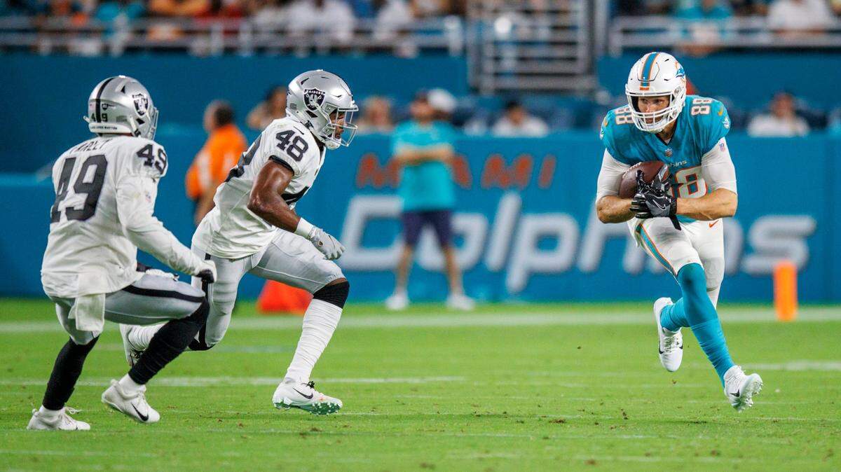 Miami Dolphins tight end Mike Gesicki (88) runs with the football against Las Vegas Raiders safety Matthias Farley (49) and Raiders cornerback Sam Webb (48) during second quarter of an NFL preseason football game at Hard Rock Stadium on Saturday, August 20, 2022 in Miami Gardens, Florida.
