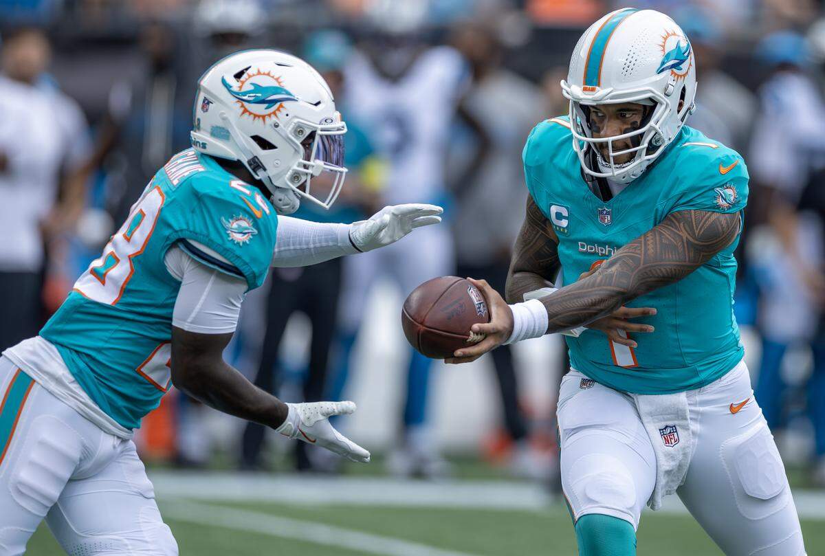 Miami Dolphins quarterback Tua Tagovailoa (1) hands off to running back De'Von Achane (28) during the first half of an NFL game against the Carolina Panthers at Bank of America Stadium on Sunday, Oct. 5, 2025, in Charlotte, N.C.