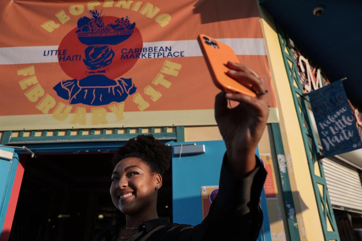 Tatiana Lozama, 29, promotions assistant for the Caribbean Marketplace, takes a proud selfie of the sign she designed for the marketplace, which is reopening after being closed for two years. The soft opening Thursday allowed vendors to get ready for a weekend of celebration.