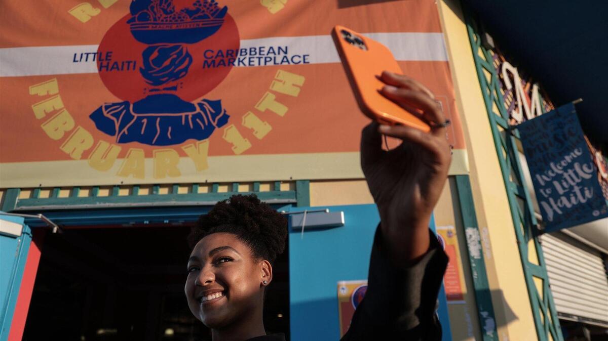 Tatiana Lozama, de 29 años,, asistente de promociones de Caribbean Marketplace, se toma una foto junto al logo que diseñó para el mercado, que abre tras dos años cerrado por la pandemia.
