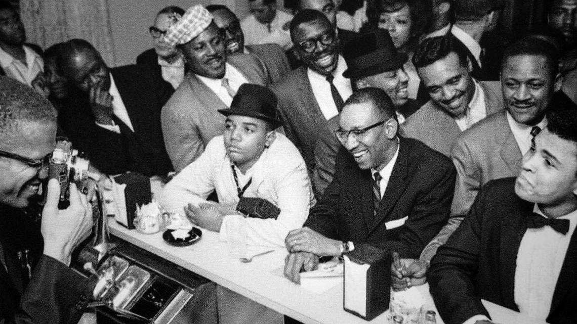 Pictured is the original photo of Malcolm X, far left, photographing Muhammed Ali, far right, inside the historic motel’s cafe that was later recreated in a scene of the upcoming new film “One Night in Miami.” Hampton House plays an important role in the new film release “One Night in Miami” the fictional account of one incredible night where icons Muhammad Ali, Malcolm X, Sam Cooke, and Jim Brown gathered discussing their roles in the civil rights movement and cultural upheaval of the 60s at historic segregation motel in Miami’s Brownville neighborhood.