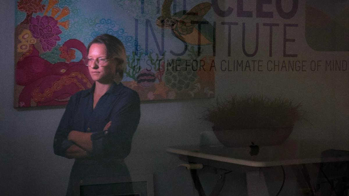 Olivia Collins has suffered from climate anxiety and is learning to cope with it while living in Miami, Collins’s reflection is cast on the glass window separating an adjacent office while standing by her desk at the CLEO Institute in Miami, Florida on Tuesday, July 30, 2024.