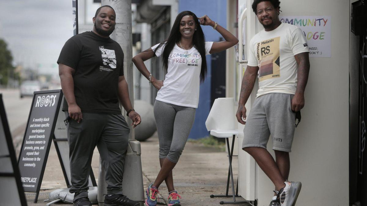 Isaiah Thomas, a la izquierda, Sherina Jones y Danny Agnew junto al refrigerador que colocaron frente a Roots Collective para ofrecer comida gratis a los vecinos.