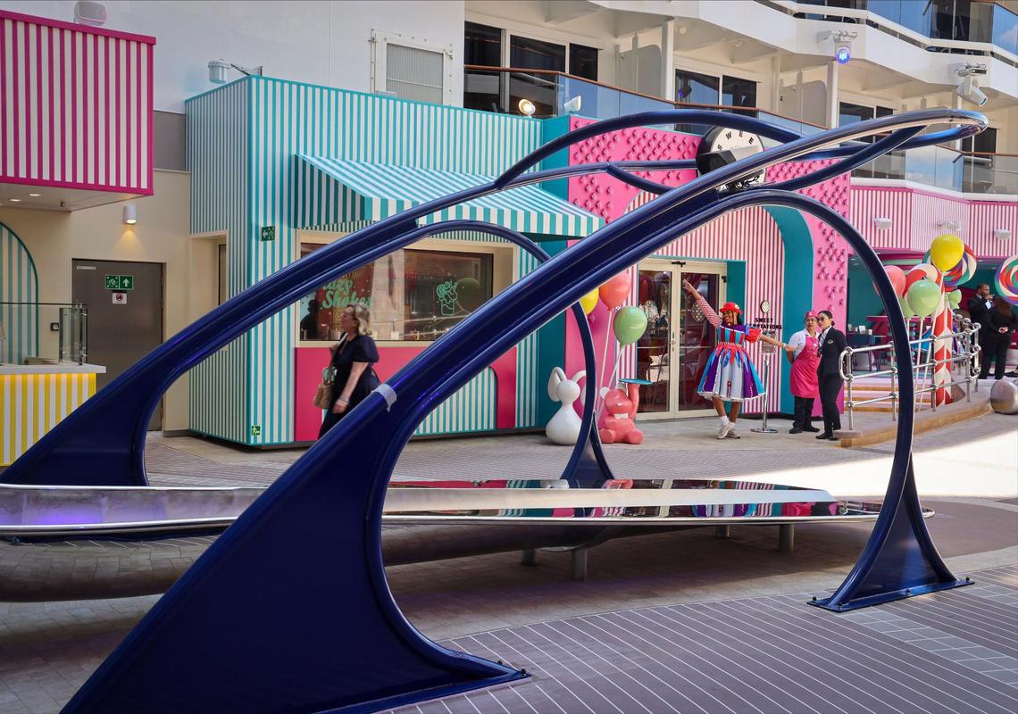 Cruise ship employee Zion John, center, gives a playful salutation to encourage visitors and travelers to venture inside Sweet Temptation, a candy store on the MSC World America.
