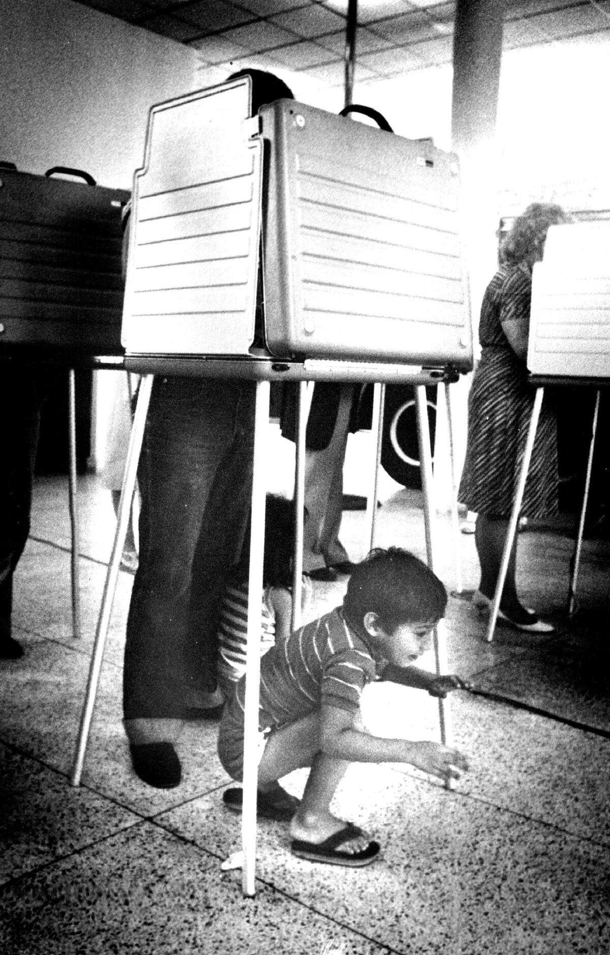 A child plays under his father’s voting both at the fire station in South Beach in 1984.