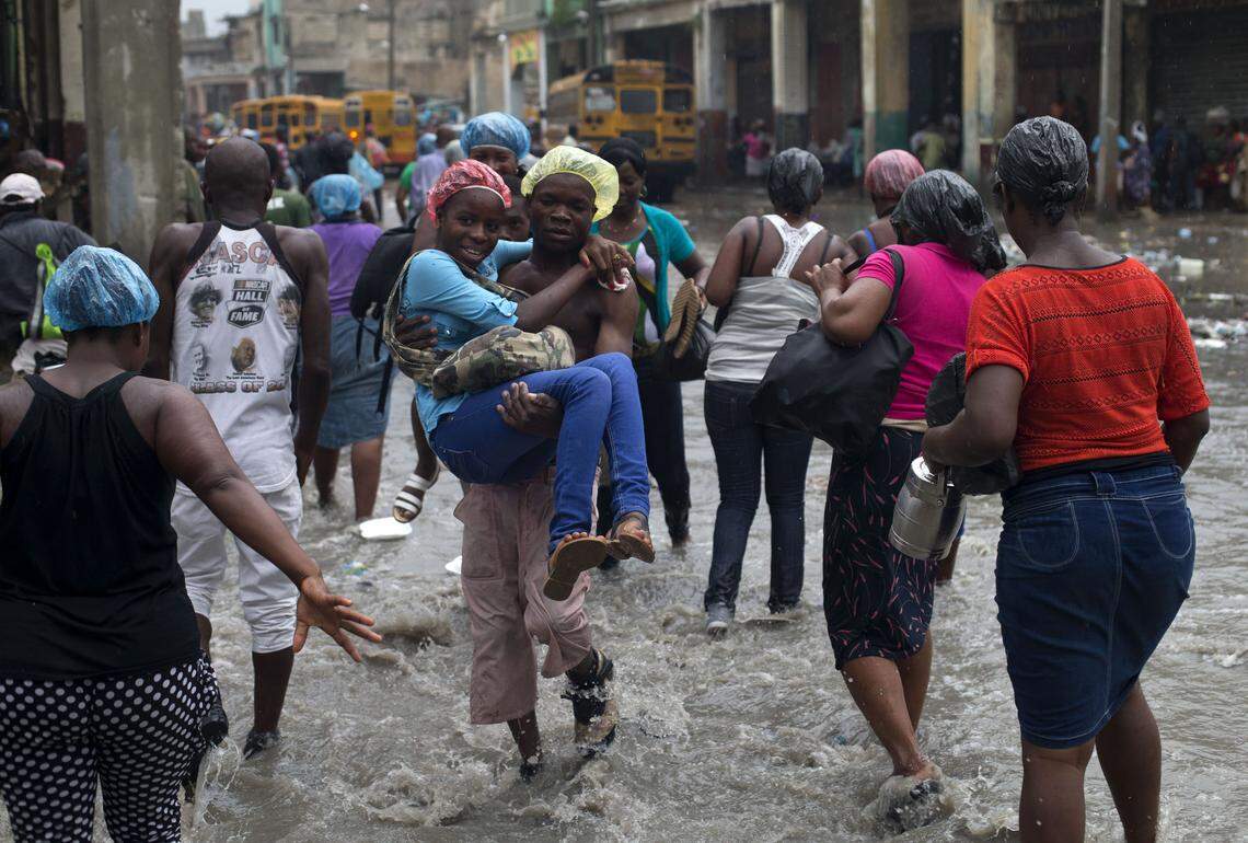 A young woman is carried across a flooded street by a man charging 5 gourdes (10 cents) for his service during a rainstorm in Port-au-Prince, Haiti, Saturday, June 20, 2015.