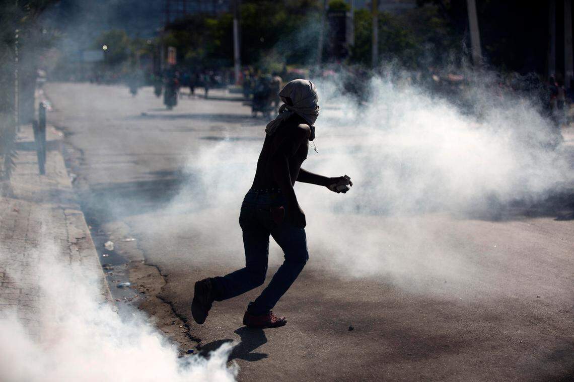 A masked protester clutching a stone runs amid tear gas launched by national police during a demonstration demanding the resignation of Haitian President Jovenel Moise near the presidential palace in Port-au-Prince, Haiti, Wednesday, Feb. 13, 2019. Protesters are angry about skyrocketing inflation and the government’s failure to prosecute embezzlement from a multi-billion Venezuelan program that sent discounted oil to Haiti. (AP Photo/Dieu Nalio Chery)