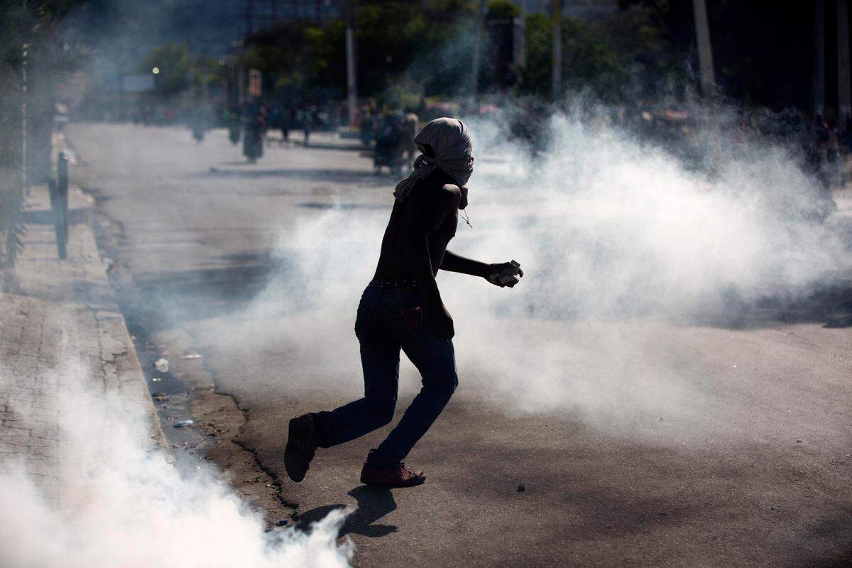 A masked protester clutching a stone runs amid tear gas launched by Haiti National Police during a demonstration demanding the resignation of Haitian President Jovenel Moise near the presidential palace in Port-au-Prince, Haiti, Wednesday, Feb. 13, 2019.