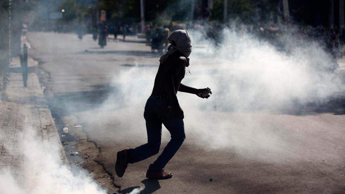 A masked protester clutching a stone runs amid tear gas launched by Haiti National Police during a demonstration demanding the resignation of Haitian President Jovenel Moise near the presidential palace in Port-au-Prince, Haiti, Wednesday, Feb. 13, 2019.