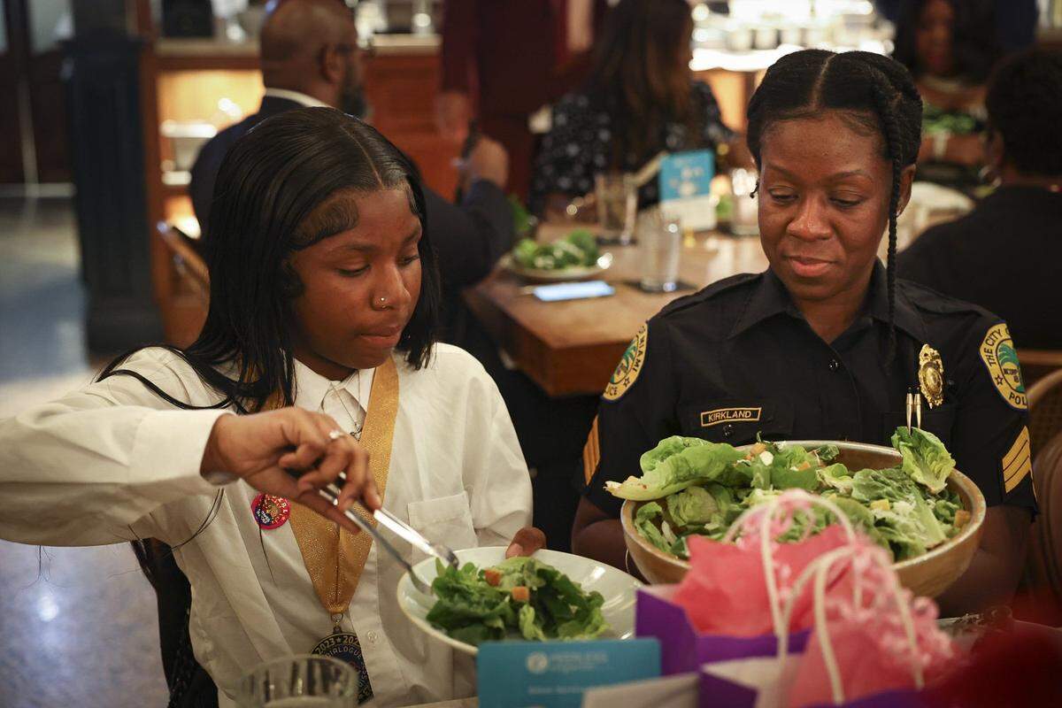 Ka’Lecia Samedy, left, uses her new etiquette skills learned in the Teen Talk mentoring program. A city of Miami police officer, one of the mentors, looks on.