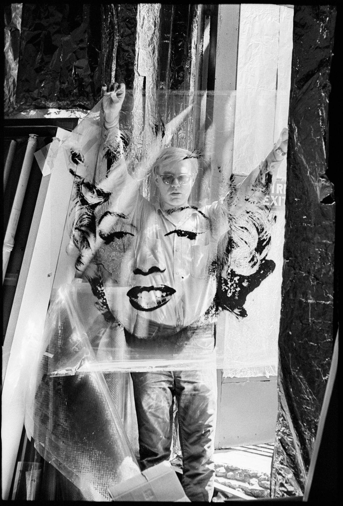 El fotógrafo William John Kennedy tomó esta imagen del artista pop Andy Warhol en Factory sosteniendo un acetato de Marilyn Monroe en 1964. La obra de arte central del vestíbulo del Andy Warhol Museum de Pittsburgh es una ampliación de esta fotografía.