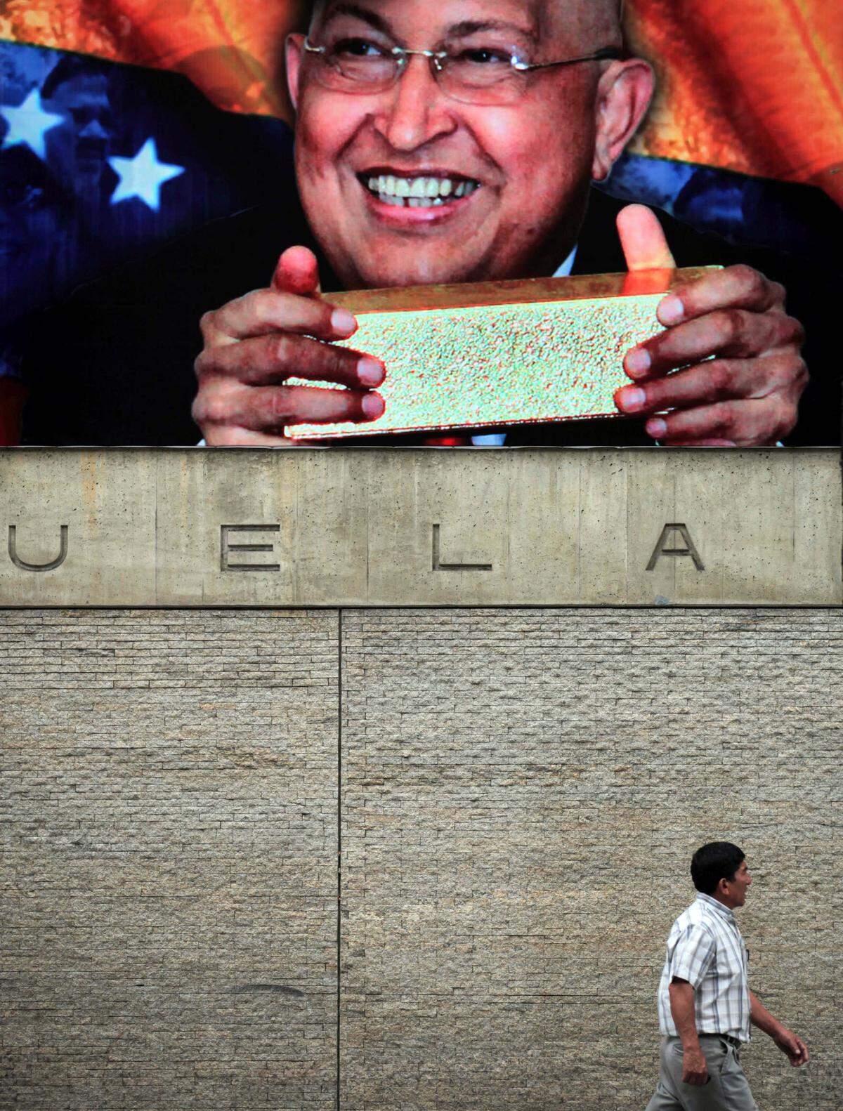A man walks by the Central Bank of Venezuela where an image hangs of Venezuela’s President Hugo Chavez holding a bar of gold in Caracas, Venezuela, March 5, 2012.