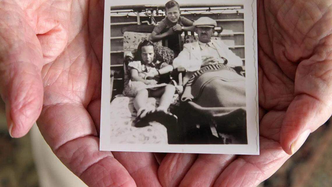 Herbert Karliner holds a photo of himself as boy, standing behind his father and a sibling aboard the ocean liner, St. Louis, in 1939,