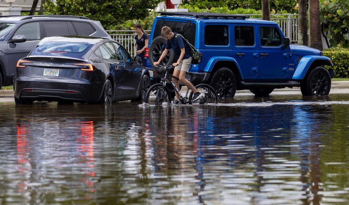 A kid rides a bicycle through floodwaters caused by a king tide and rain after school dismissal at the intersection of North Bay Road and 180th Drive in Sunny Isles Beach, Fla., Wednesday, Oct. 8, 2025.