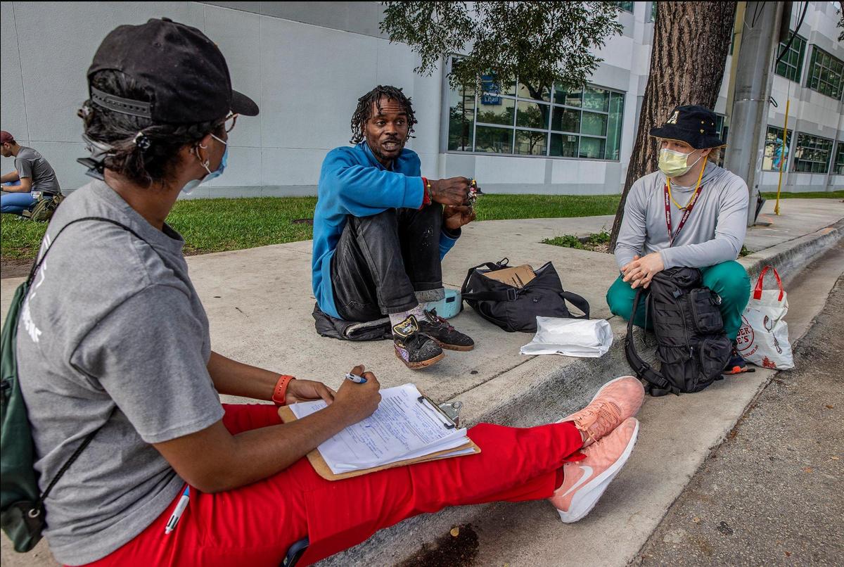 University of Miami medical students Brittany Blake, left, and Kavan Molly, right, members of Miami Street Medicine, speak to a patient named Ronald during their weekly rounds along Northwest 17th Street in Miami, on Saturday March 5, 2022.